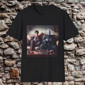 May include: Black t-shirt featuring a humorous image of Harry Potter and Voldemort playing video games. The image shows the two characters sitting on a couch, holding controllers, with a table of snacks in front of them. A fun, pop culture themed tee.