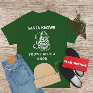 May include: Green t-shirt with a white graphic of Santa Claus and the text "Santa Knows You've Been a Knob".