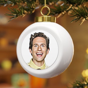 May include: White ceramic Christmas ornament with a round image of a man with brown hair and a yellow shirt. The man is smiling and looking at the camera.
