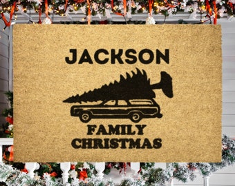 May include: A brown doormat with the text "JACKSON FAMILY CHRISTMAS" and a black silhouette of a car with a Christmas tree on top.