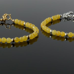 May include: Two bracelets with yellow beads and silver clasps. The bracelet on the left has a gold clasp.