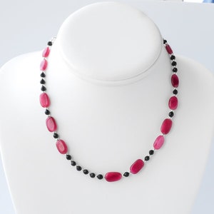 May include: A pink and black beaded necklace with oval-shaped pink beads and round black beads.