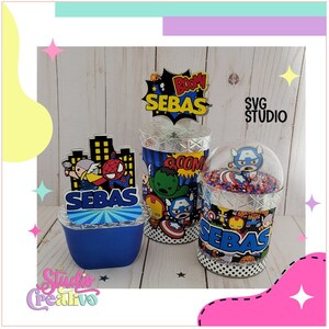 Puede incluir: Tres contenedores de favores de fiesta decorados con un tema de superhéroes. Los contenedores son azules, plateados y transparentes. Cada contenedor tiene un personaje de superhéroe diferente. Los contenedores están etiquetados con el nombre "Sebas".