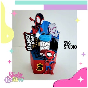 Op de afbeelding: Een rode, blauwe en zwarte kartonnen feestgunstdoos met een Spiderman-thema. De doos heeft een Spiderman-personage, een Spiderman-personage met een zwart pak en een wit Spiderman-personage. De doos heeft een doorzichtige plastic container met een blauwe deksel. De doos heeft de tekst "HENRY KIMO" en "SVG STUDIO" erop gedrukt.