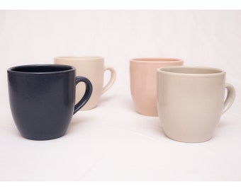 Peut inclure: Quatre tasses en céramique de différentes couleurs : noir, beige, brun clair et rose. Les tasses ont une forme arrondie et une anse.