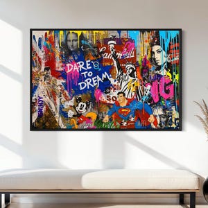 Könnte beinhalten: Ein gerahmter Pop-Art-Druck mit schwarzem Rand, der eine Collage ikonischer Figuren und die Worte "DARE to DREAM" zeigt. Das Kunstwerk enthält Bilder von Mona Lisa, Superman und Mickey Mouse mit lebendigen Farbspritzern.