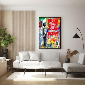 K&ouml;nnte beinhalten: Ein farbenfroher abstrakter Kunstdruck mit einer jungen Person, die vor einer Wand mit den Worten "Dream Big Dreams" in roter Farbe steht.