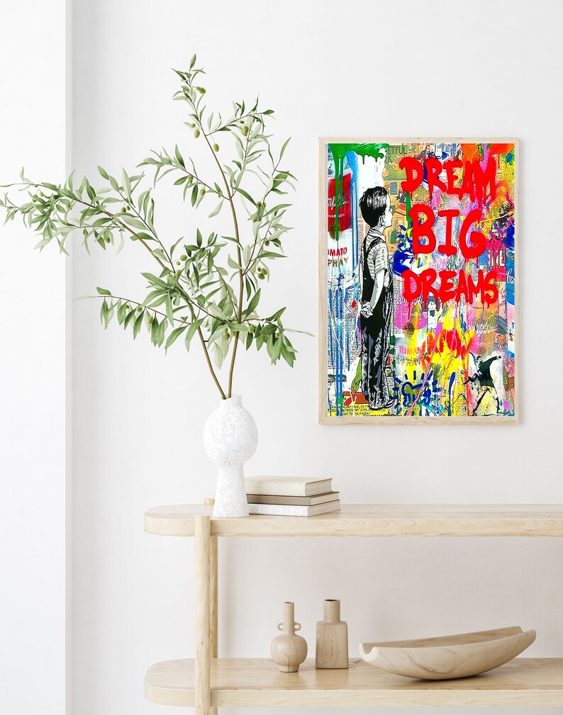 K&ouml;nnte beinhalten: Ein farbenfroher abstrakter Kunstdruck mit einer jungen Person, die vor einer Backsteinmauer steht. Der Druck zeigt die Worte "Dream Big Dreams" in roter Farbe.
