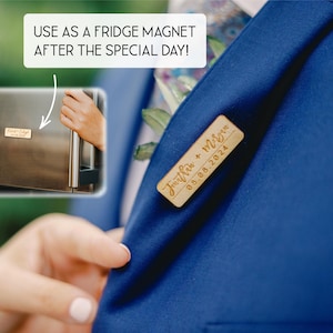 May include: A rectangular light wood pin featuring the engraved names Jonathan + Megan and the date 08.08.2024, attached to a blue fabric lapel. An inset shows the same wooden piece functioning as a fridge magnet with the text USE AS A FRIDGE MAGNET AFTER THE SPECIAL DAY!