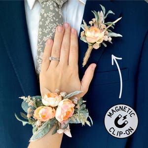 May include: A navy blue suit jacket with a floral boutonniere and wrist corsage. The boutonniere is pinned to the lapel, and the wrist corsage is worn on the wrist. Both floral arrangements feature peach-colored flowers and greenery. A magnetic clip-on is also visible.