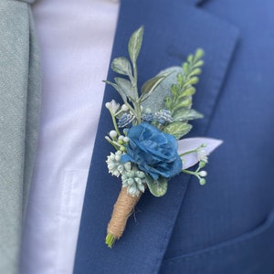 Puede incluir: Un boutonniere floral azul y verde con una rosa azul y vegetación.