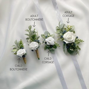 K&ouml;nnte beinhalten: Vier wei&szlig;e Blumen-Boutonni&egrave;res und Corsagen mit Gr&uuml;n und blauen Akzenten. Der Text "Erwachsene Boutonniere", "Erwachsene Corsage", "Kind Boutonniere" und "Kind Corsage" ist auf dem Bild zu sehen.
