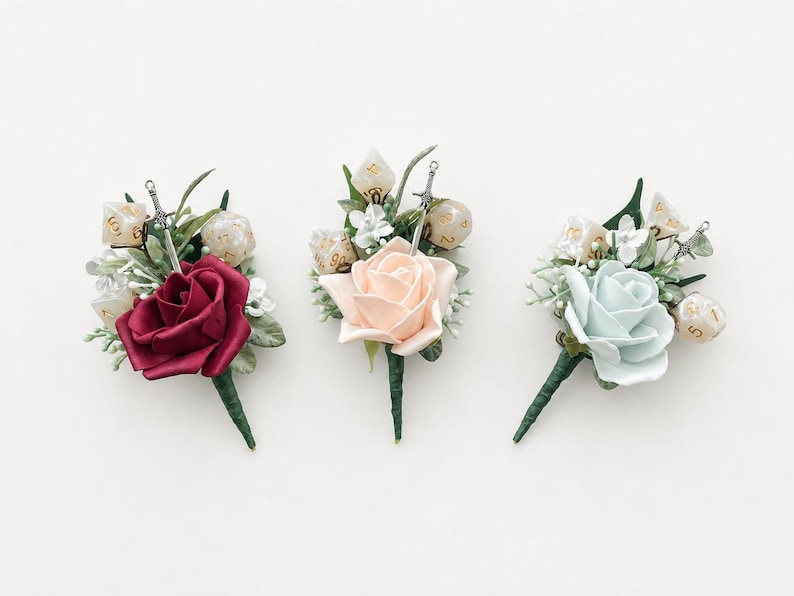 May include: Three floral boutonnieres featuring a single rose in deep red, pale peach, or light blue. Each arrangement includes green foliage, small white flowers, polyhedral dice with gold numbering, and a miniature silver sword charm.