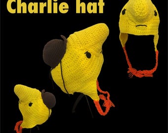 May include: Yellow crocheted hat with brown ear flaps and orange ties. The hat has a face design with black eyes and a stitched mouth. The text "Charlie hat" is displayed in yellow.