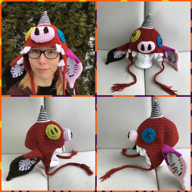 May include: A red, white, and black crocheted hat with a pig face and horns. The hat has a long tail with a tassel. The hat is on a white mannequin head.
