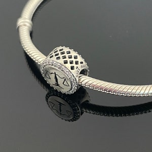 May include: A silver charm bracelet with a silver charm featuring a scale of justice design. The charm is engraved with "925 ALE".