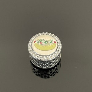 May include: A silver charm with a hot dog and toppings on a white background. The charm is surrounded by clear crystals.
