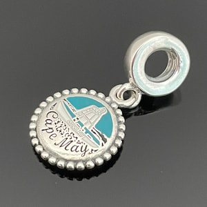 May include: Silver charm with a blue and white enamel design of the Cape May Lighthouse. The charm has a silver ring for attaching to a bracelet.