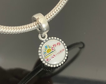 May include: Silver charm with a white enamel circle featuring a colorful sunset and palm trees with the text "St. Maarten".
