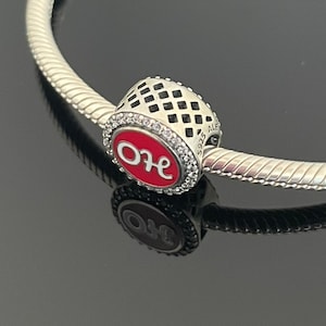 Peut inclure: Bracelet de charme en argent avec un charme rouge et blanc qui dit "OU". Le charme a un motif à carreaux noir et blanc autour du bord.