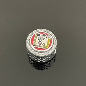 Op de afbeelding: Zilveren bedel met een rood, geel en wit geëmailleerd Mickey Mouse-ontwerp. De bedel is omgeven door een cirkel van heldere zirkonia-stenen.