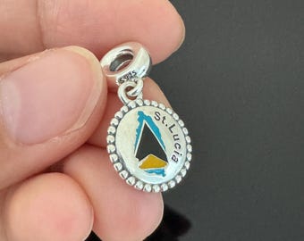 May include: Silver charm with a blue, yellow, and black enamel design of the island of St. Lucia. The charm has a beaded border and a silver loop for attaching to a bracelet.