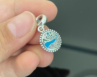May include: Silver charm with a blue, green, and yellow enamel design of a palm tree and beach scene. The charm has a silver bead border and the text "St. Lucia" in black.