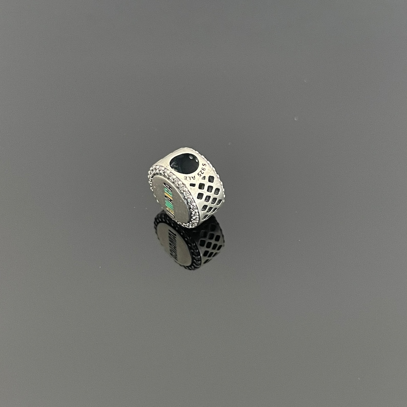 May include: Silver charm with a heart-shaped cutout and a patterned design. The charm has a small inscription that reads "925 ALE".