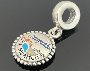 May include: Silver charm with a blue, white, and orange enamel design of an airplane flying over a small island with the text "St. Maarten".
