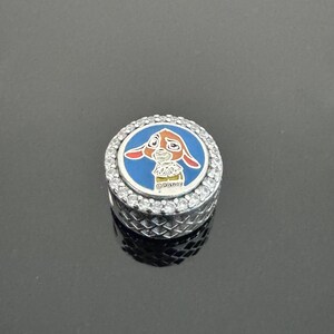 Puede incluir: Un charm de plata con un dise&ntilde;o de esmalte azul y blanco con un conejo de dibujos animados. El charm est&aacute; rodeado de piedras redondas y transparentes y tiene la palabra "Disney" impresa.