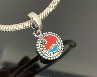 May include: Silver charm bracelet with a silver charm featuring a red, blue, and yellow sunset with palm trees and the text "St. Maarten".
