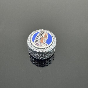 Puede incluir: Un charm redondo plateado con un dise&ntilde;o de esmalte azul y blanco. El charm presenta un retrato de una mujer con pelo largo. El charm est&aacute; incrustado con peque&ntilde;os cristales transparentes alrededor del borde.