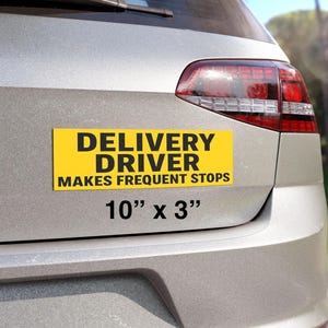 以下が含まれることがあります： 「DELIVERY DRIVER MAKES FREQUENT STOPS」と黒い文字で書かれた黄色の長方形のバンパーステッカー。ステッカーのサイズは長さ25.4cm、高さ7.6cmで、銀色の車の後部に貼られています。