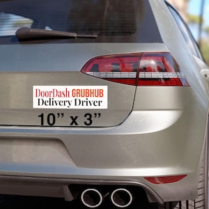 Może przedstawiać: Biała prostokątna naklejka na tylnej części srebrnego samochodu. Naklejka zawiera napis "DoorDash GRUBHUB Delivery Driver" w kolorze czerwonym i czarnym. Poniżej znajduje się wymiar "10" x 3"" (25,4 cm x 7,6 cm) w kolorze czarnym.