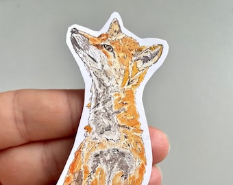 May include: A watercolor sticker of a fox with orange and white fur, sitting on green grass. The fox is looking upwards with a curious expression. The sticker has a white border.