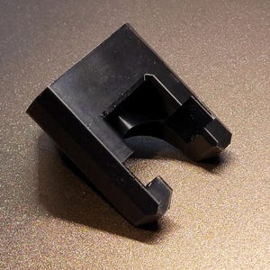 May include: A black, angular, 3D-printed object with a distinctive shape. It features a rectangular base and a curved, open section. The surface shows layer lines from the printing. This appears to be a custom-made component.