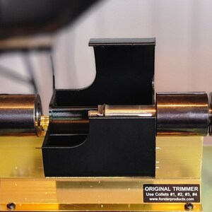 May include: A black metal tool with a gold base and a silver handle. The tool has a black plastic housing with a silver metal rod inside. The tool is labelled "ORIGINAL TRIMMER" and "Use Collets #1, #2, #3, #4" with the website "www.forsterproducts.com".