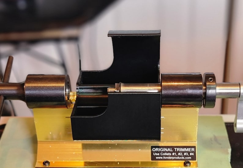 May include: A black metal tool with a gold base and a silver handle. The tool has a black plastic housing with a silver metal rod inside. The tool is labelled "ORIGINAL TRIMMER" and "Use Collets #1, #2, #3, #4" with the website "www.forsterproducts.com".