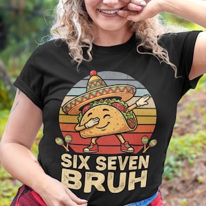 Puede incluir: Camiseta negra con un taco de dibujos animados con sombrero y haciendo un dab. El taco sonríe y lleva zapatillas rojas. El diseño incluye maracas y el texto "SIX SEVEN BRUH" en un estilo vintage.