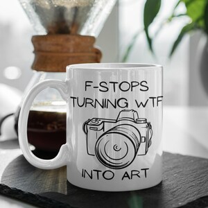 May include: White ceramic mug with a black and white illustration of a camera and the text "F-Stops Turning WTF Into Art".