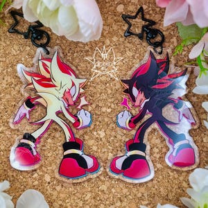 May include: Two acrylic keychains featuring a stylized character in a dynamic pose. One keychain displays the character in cream and red, while the other shows the character in black and red. Both include black star-shaped clasps and the text dokilbi.