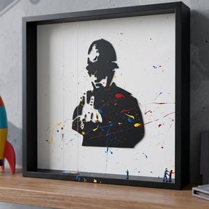 May include: Black framed art print featuring a silhouette of a person with colorful paint splatters. The artwork is displayed on a wooden shelf with a toy rocket and video game cartridges. The art print has the words "Urban Shadows" in the bottom right corner.