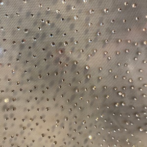 Può includere: Uno sfondo in tessuto bianco con un motivo di piccoli strass trasparenti.