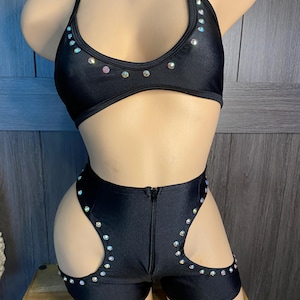 May include: Black two-piece halter top and shorts set. The halter top and shorts are embellished with iridescent rhinestones. The shorts have cut-out details on the sides and a front zipper. The set is displayed on a mannequin.