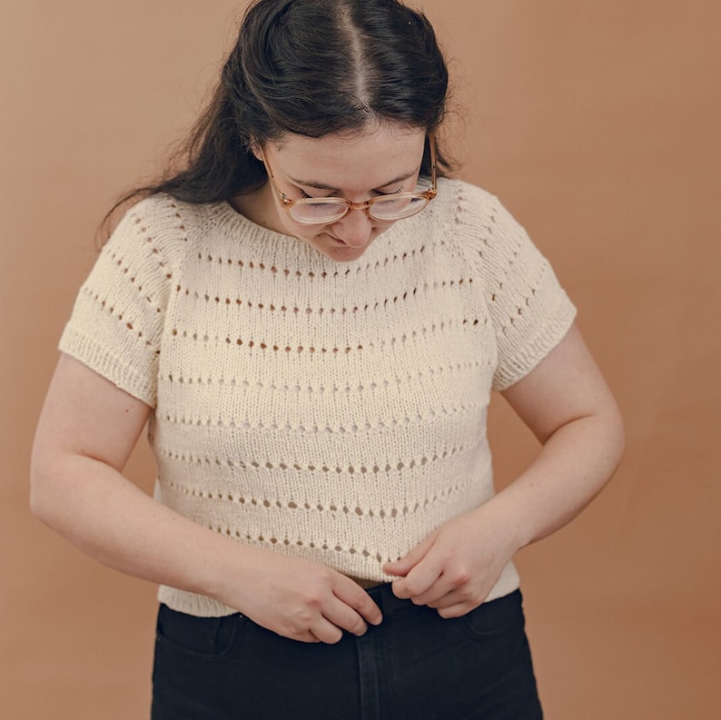 May include: A white crocheted top with a delicate openwork pattern. The top has short sleeves and a round neckline.