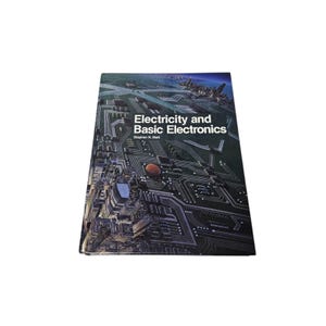 May include: A hardcover book titled "Electricity and Basic Electronics" by Stephen R. Matt. The cover features a detailed illustration of a circuit board with a cityscape in the background. The book is set against a white background.