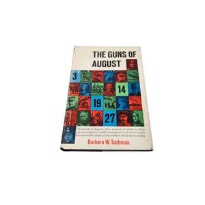 May include: A hardcover book titled "The Guns of August" by Barbara W. Tuchman. The cover features a grid of images and the dates 3, 14, 19, and 27. The book's description details the events of August 1914.