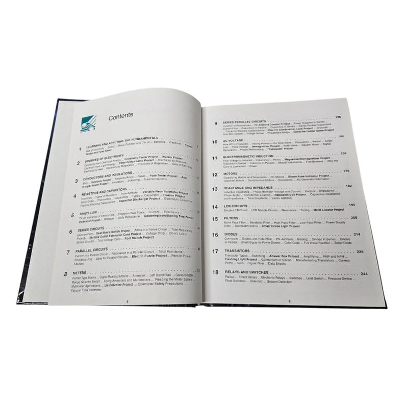 May include: An open book with a dark blue cover, displaying a table of contents. The text includes titles such as "Learning and Applying the Fundamentals", "Sources of Electricity", and "Series Circuits".