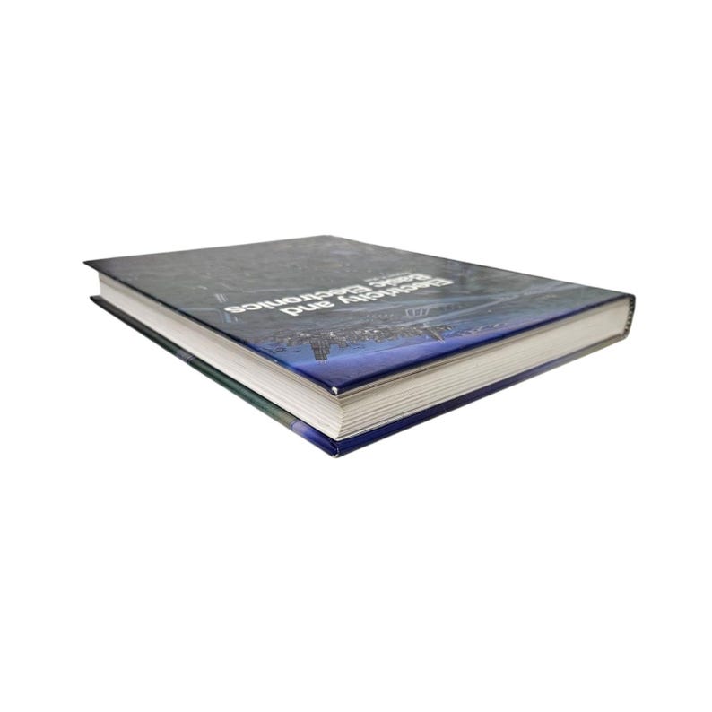 May include: A hardcover book titled "Electricity and Basic Electronics" with a dark blue cover. The cover features a cityscape silhouette and white text. The book is lying on a white surface.