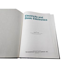 May include: An open book with the title "Electricity and Basic Electronics" in green text. The author's name and publisher's information are also visible. The book's pages are white, and the cover is black.